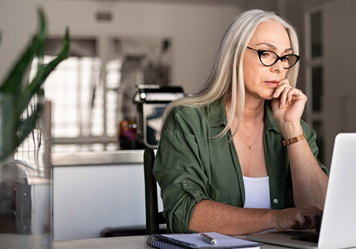 Focused old woman at home using laptop.